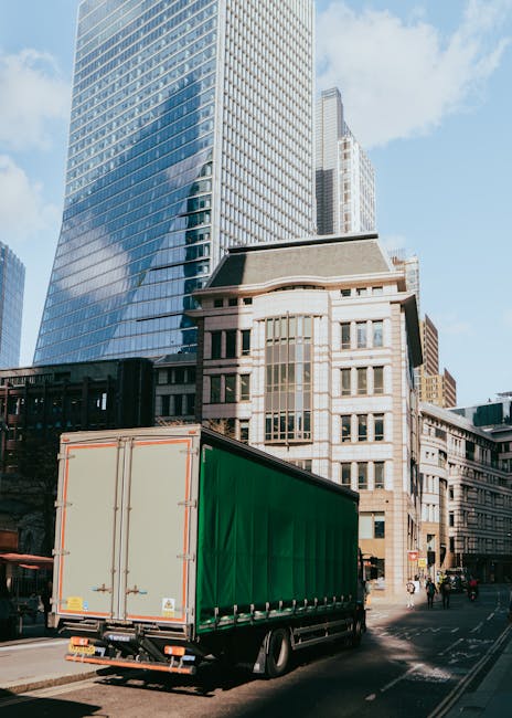 A flatbed truck from Man with Van Haggerston is parked in the middle of a busy street in Haggerston, with a white van positioned behind it during a home relocation process. The flatbed is loaded with 